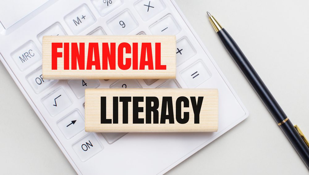  Wooden blocks with the text FINANCIAL LITERACY lie on a light background on a white calculator. Nearby is a black handle. Business concept 