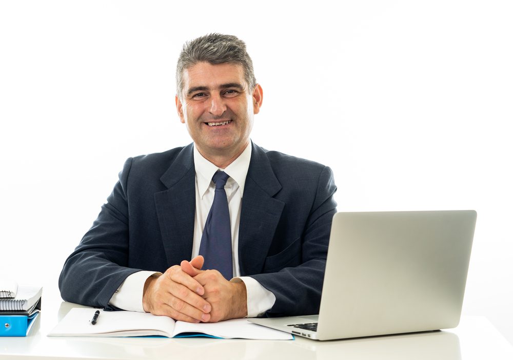 Attractive happy mature caucasian businessman working on laptop computer on desk at office  